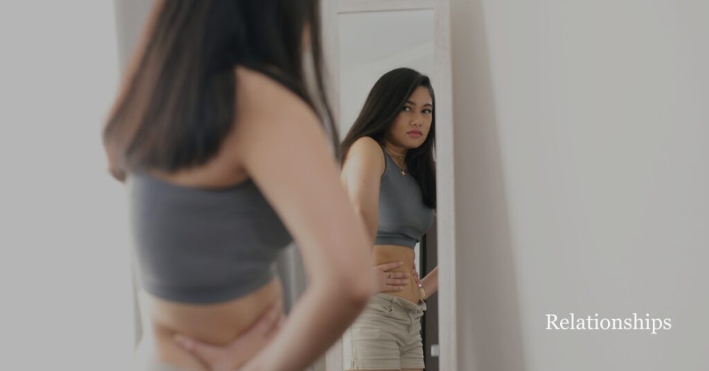 woman looking in mirror holding stomach dealing with body image anxiety